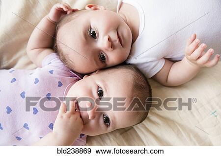 Caucasian twin baby girls laying on bed View Large Photo Image Stock Photo - Caucasian twin baby girls laying on bed. Fotosearch