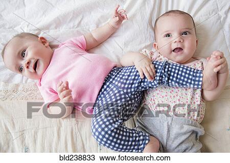 Stock Image - Caucasian twin baby girls playing on bed. Fotosearch