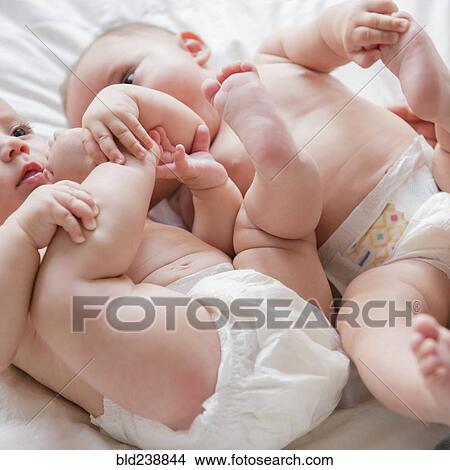 Picture - Caucasian twin baby girls wearing diapers on bed. Fotosearch