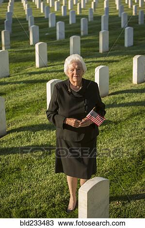 Stock Image - Caucasian widow holding American flag in cemetery. Fotosearch