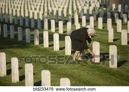 Stock Photo - Caucasian widow placing American flag at cemetery gravestone. Fotosearch