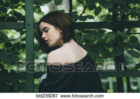 Stock Photo - Caucasian woman baring shoulder near foliage. Fotosearch