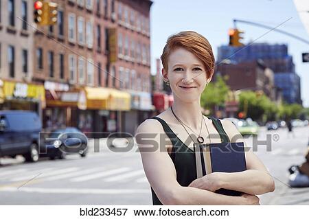 Stock Photo - Caucasian woman carrying books on city sidewalk. Fotosearch