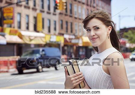 Stock Photo - Caucasian woman carrying books on city sidewalk. Fotosearch