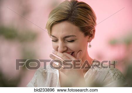 Stock Photograph - Caucasian woman covering mouth while laughing. Fotosearch