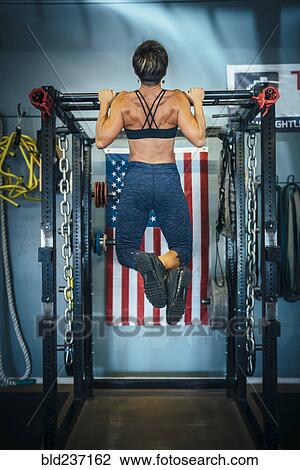 Stock Image - Caucasian woman doing chin-up in gymnasium . Fotosearch
