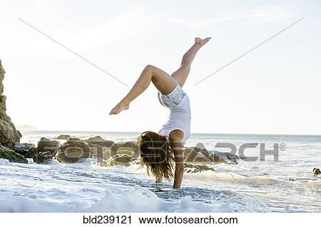 Stock Image - Caucasian woman doing handstand on beach. Fotosearch