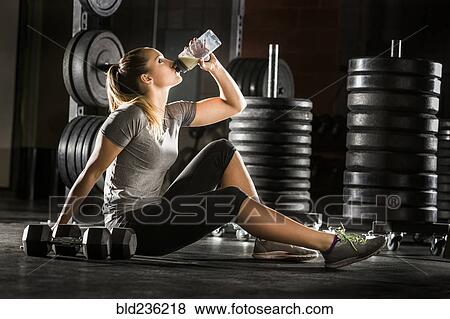 Caucasian woman drinking juice on floor in gymnasium View Large Photo Image Stock Photo - Caucasian woman drinking juice on floor in gymnasium. Fotosearch