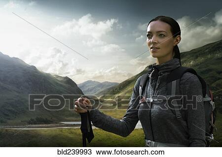 Stock Image - Caucasian woman hiking in green valley. Fotosearch