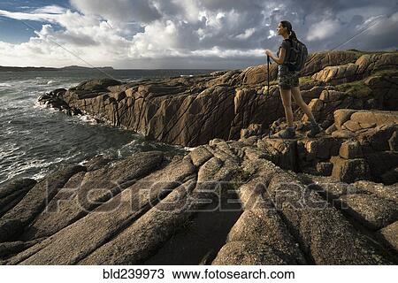Stock Image - Caucasian woman hiking on rocks near ocean. Fotosearch