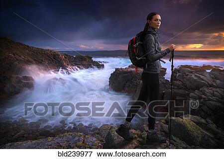 Stock Photo - Caucasian woman hiking on rocks near ocean. Fotosearch