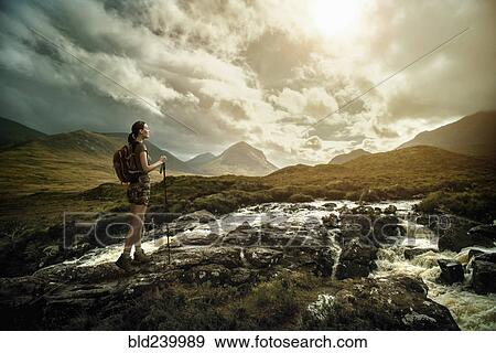 Stock Photo - Caucasian woman hiking on rocks near river. Fotosearch