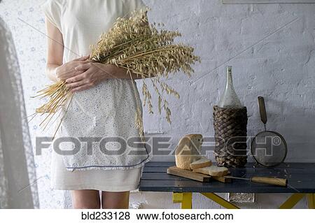 Stock Photo - Caucasian woman holding bouquet of wheat near sliced bread. Fotosearch