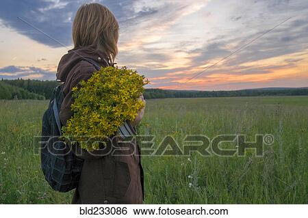Stock Photograph - Caucasian woman holding bouquet of flowers in field at sunset. Fotosearch