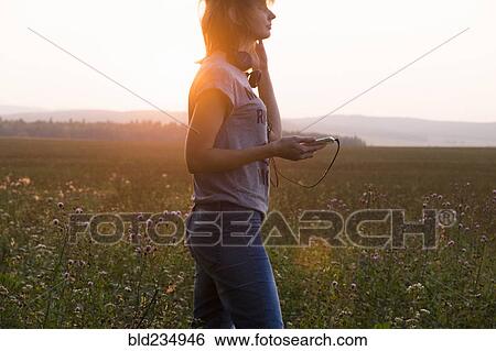 Stock Photograph - Caucasian woman holding cell phone standing in field. Fotosearch