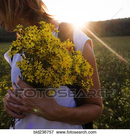Stock Photo - Caucasian woman holding flowers in sunny field. Fotosearch