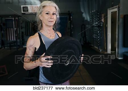 Stock Photo - Caucasian woman holding large weight in gymnasium. Fotosearch