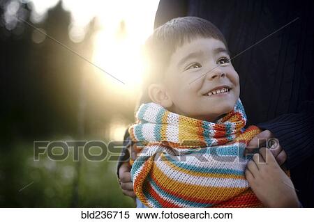 Stock Photography - Caucasian woman holding shoulders of boy wearing multicolor scarf. Fotosearch