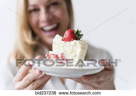 Stock Photo - Caucasian woman holding slice on vanilla cake with strawberry. Fotosearch