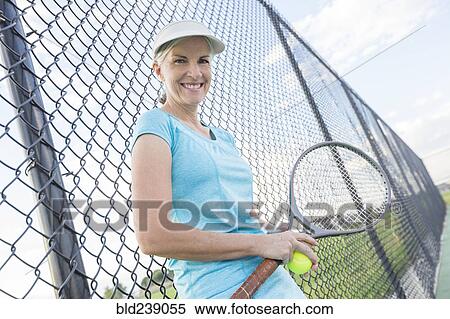 Stock Photography - Caucasian woman holding tennis racket leaning on fence. Fotosearch