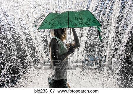Stock Photo - Caucasian woman holding umbrella near splashing water. Fotosearch