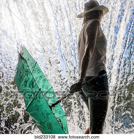 Stock Photo - Caucasian woman holding umbrella near splashing water. Fotosearch