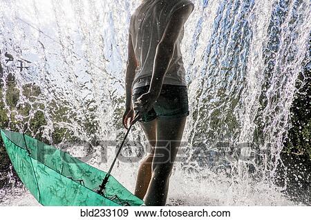 Stock Photo - Caucasian woman holding umbrella near splashing water. Fotosearch