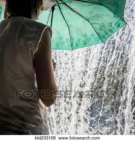 Stock Photograph - Caucasian woman holding umbrella near splashing water. Fotosearch