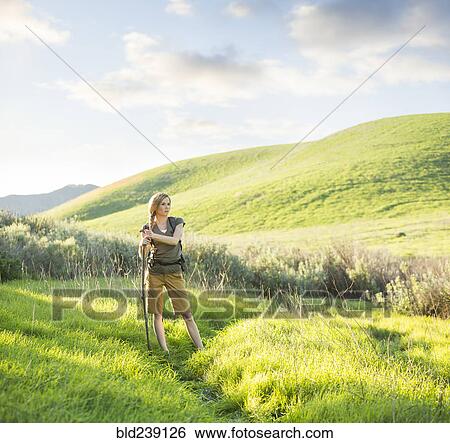 Stock Photograph - Caucasian woman holding walking stick on hill. Fotosearch