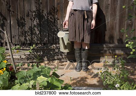 Stock Image - Caucasian woman holding watering can in garden. Fotosearch