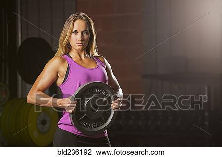 Stock Image - Caucasian woman holding weight in gymnasium. Fotosearch