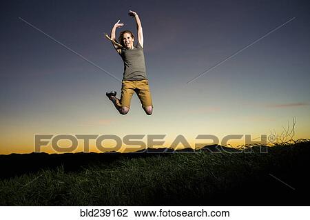 Stock Image - Caucasian woman jumping for joy at sunset. Fotosearch