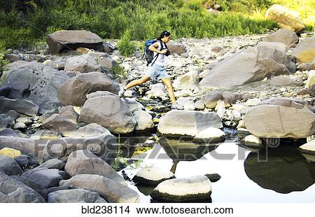Picture - Caucasian woman jumping on rocks in river. Fotosearch