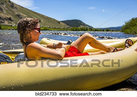 Stock Image - Caucasian woman laying in inflatable raft texting on cell phone. Fotosearch
