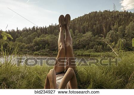 Stock Photo - Caucasian woman laying near river with legs raised. Fotosearch