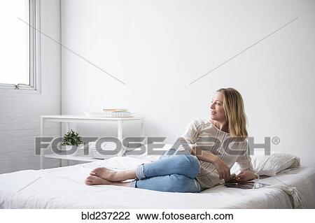 Stock Image - Caucasian woman laying on bed looking at window. Fotosearch