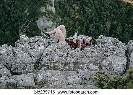 Stock Photography - Caucasian woman laying on mountain rocks reading magazine. Fotosearch
