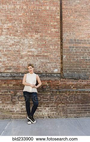 Stock Image - Caucasian woman leaning on brick wall. Fotosearch