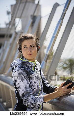 Caucasian woman leaning on bridge railing listening to earbuds View Large Photo Image Picture - Caucasian woman leaning on bridge railing listening to earbuds. Fotosearch