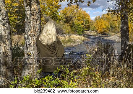 Stock Image - Caucasian woman leaning on tree near river. Fotosearch