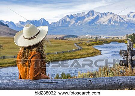 Stock Image - Caucasian woman leaning on wooden fence near mountain river. Fotosearch