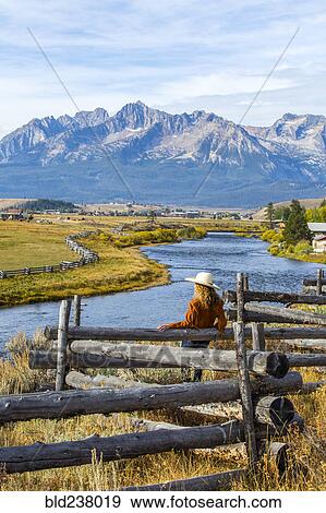 Stock Photo - Caucasian woman leaning on wooden fence at mountain river. Fotosearch