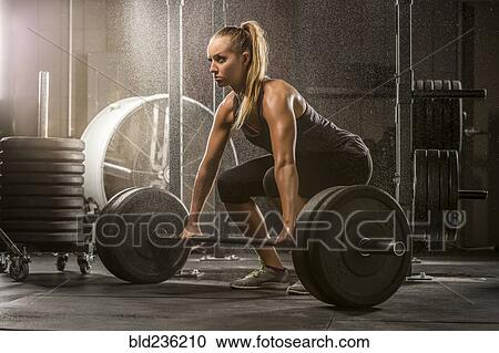 Stock Image - Caucasian woman lifting barbell in gymnasium. Fotosearch