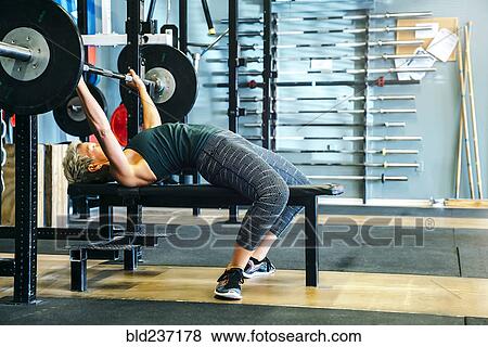 Caucasian woman lifting barbell on bench in gymnasium View Large Photo Image Stock Photo - Caucasian woman lifting barbell on bench in gymnasium. Fotosearch