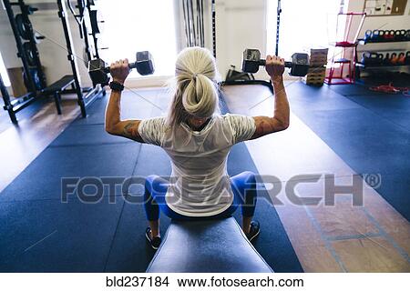 Picture - Caucasian woman lifting dumbbells in gymnasium. Fotosearch