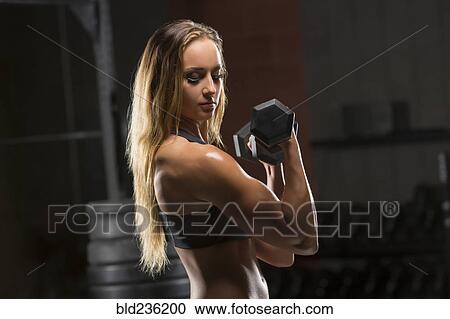 Stock Image - Caucasian woman lifting dumbbells in gymnasium. Fotosearch