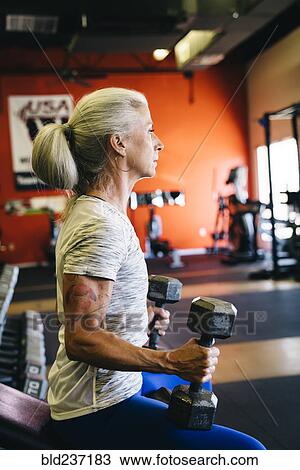 Stock Image - Caucasian woman lifting dumbbells in gymnasium. Fotosearch