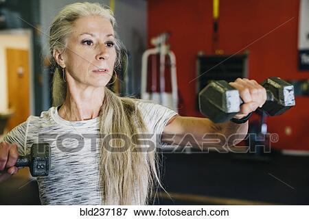 Stock Photo - Caucasian woman lifting dumbbells in gymnasium. Fotosearch