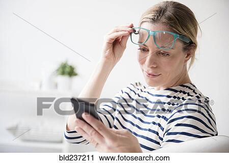 Caucasian woman lifting eyeglasses reading cell phone View Large Photo Image Stock Image - Caucasian woman lifting eyeglasses reading cell phone. Fotosearch