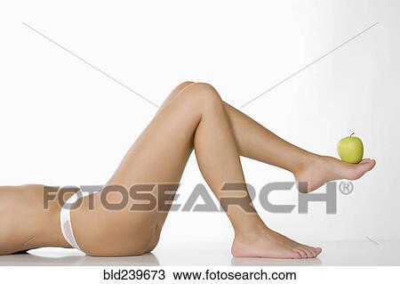 Stock Image - Caucasian woman lifting green apple with foot. Fotosearch